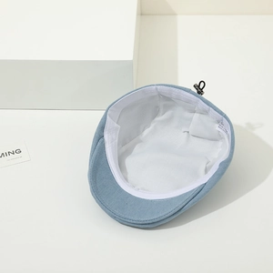 Detail of light blue denim baby flat cap showing white lining and cotton wash label