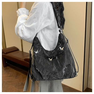 Model wearing large black pleated shoulder bag with silver butterfly pendants detail