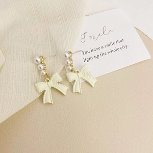 Detail of long drop bow earrings with cream pearls and gold-plated textured ribbons