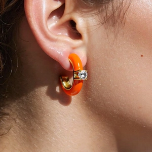Detail view of orange C-shaped enamel hoop earring with sparkling zircon on ear