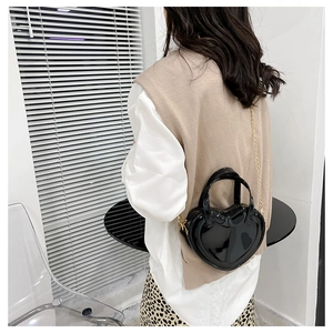 Glossy black heart-shaped handbag with gold chain strap shown on a model's shoulder