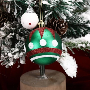 Close-up of green Christmas ball with glitter patterns hanging on a snowy tree