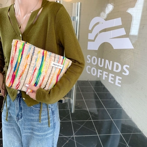 Detail of colorful striped knitted pouch held by a model in a minimalist street setting