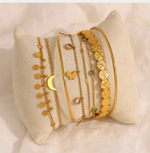 Detail view of gold layered bracelets with moon and flower pendants on white display pillow