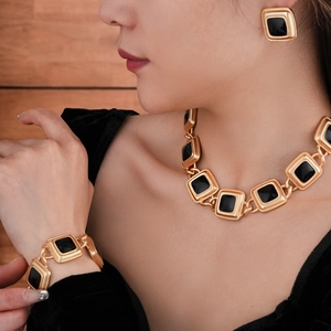 Detail of vintage gold jewelry set with black square enamel on a warm wood background