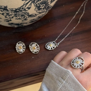 Detailed view of silver daisy jewelry set with necklace and earrings on wooden surface