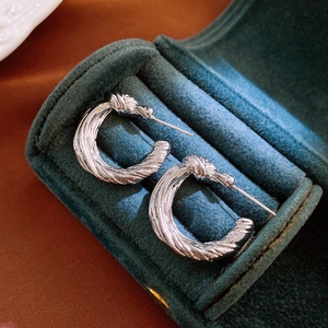 Detailed macro view of silver knotted C-shaped hoop earrings on dark green velvet cushion