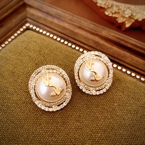 Detailed close-up of golden pearl earrings with crystal inlay on olive green textile
