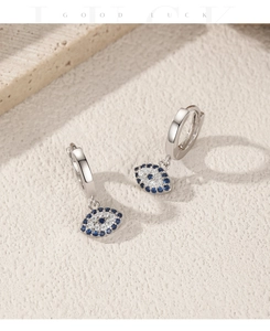 Macro detail of silver evil eye earrings featuring sparkling blue and white crystals
