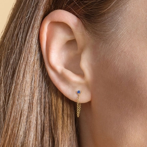 Macro shot of gold chain drop earrings with blue cubic zirconia on earlobe