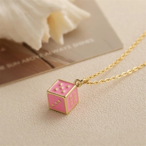 Collana dorata con ciondolo a dado in smalto rosa su un'elegante superficie beige