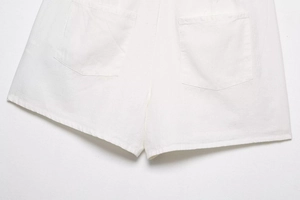 Detail view of white cotton-linen shorts showing back pockets and hem stitching texture