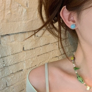 Detail view of blue crystal flower stud earrings worn with a colorful beaded necklace
