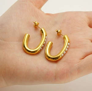 Detail of U-shaped gold earrings with embedded pearls held in hand for size reference