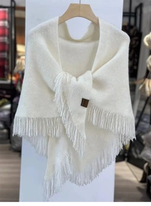 Detailed view of white knit wool shawl featuring tassel fringe and small brown leather label
