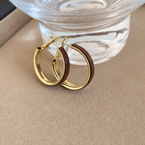 Detailed macro view of gold hoop earrings with dark brown velvet texture and silver needles