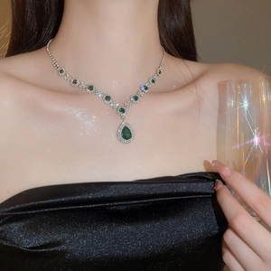 Close-up of elegant emerald waterdrop pendant necklace on model in black evening dress