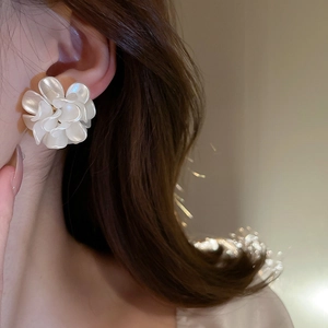 Elegant white acrylic flower stud earrings with pearl luster on a female model