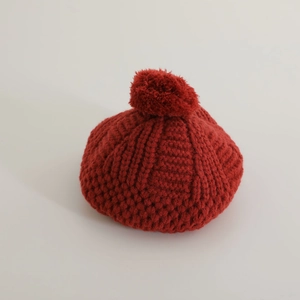 Détail du béret tricoté rouge avec texture en laine épaisse et pompon assorti doux