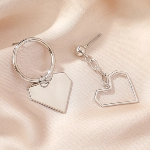 Detailed view of silver asymmetric heart earrings on champagne satin background