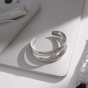Close-up of minimalist silver triple-layered open cuff bracelet on a modern desk setup