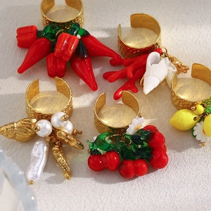 Dettaglio di anelli placcati oro con ciondoli a ciliegia, limone e corallo su texture
