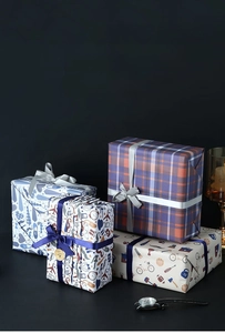 Detail of luxury gift wrapping paper featuring plaid and necktie patterns with silk ribbons