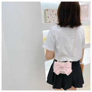 Detail view of pink bow crossbody bag with pearl handle and metal chain on model