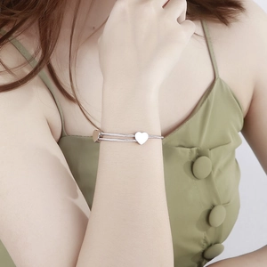 Close-up of heart charm on minimalist silver double-wire stainless steel cuff bracelet