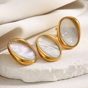 Detail of 18K gold plated oval earrings and ring with mother of pearl on a textured stone