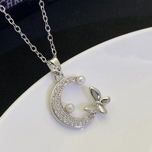 Macro shot of silver crescent moon and butterfly pendant with zircons and small pearls