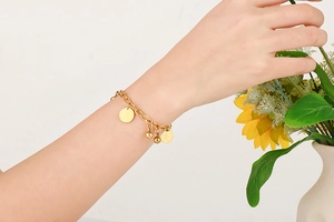 Dettaglio di un bracciale vintage in acciaio dorato con ciondoli a moneta sul polso di un modello