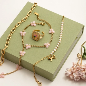 Detail of gold flower bracelets and rings with pink butterfly charms on green gift box