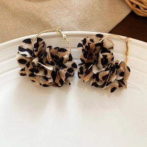 Close-up of leopard print fabric flower earrings with gold metal hoops on white ceramic
