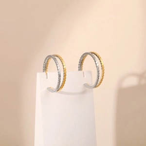 Two-tone gold and silver layered hoop earrings with textured hammered finish on a stand