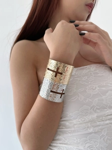 Detail of wide hammered metal cuffs featuring a cutout cross design in gold and silver