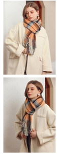 Detail of soft orange and grey plaid scarf featuring decorative fringe tassels