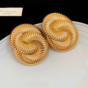 Macro detail of golden geometric double spiral earrings with textured finish on white plate