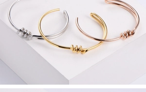 Detailed close-up of knotted titanium steel bangles in silver, gold, and rose gold finishes
