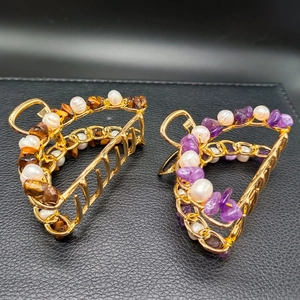 Detailed view of gold hair claws featuring natural amethyst stones and pearls on black texture