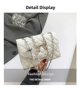 Detail of white quilted handbag with golden bow accent and chain strap against suit fabric