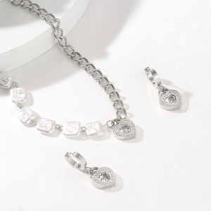 Macro shot of silver heart-shaped gemstone pendant with pearl chain necklace and earrings