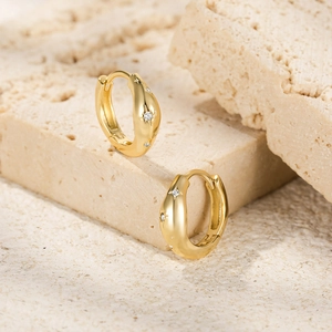 Detail of gold starburst hoop earrings with sparkling zircons on beige stone