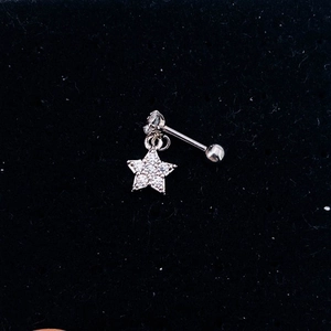 Macro shot of silver star-shaped cartilage earring with zircon on black velvet