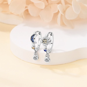 Silver celestial sun and moon earrings with blue and yellow gemstones on floral background