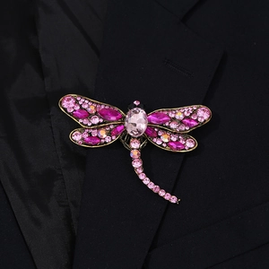 Detailed close-up of a luxury dragonfly brooch with pink crystals on a black suit blazer