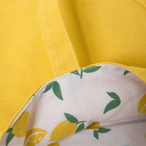 Yellow canvas tote bag showing handle stitching and lemon print lining detail