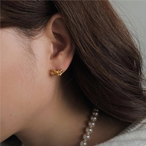 Close-up of elegant gold bow stud earrings worn by a model with pearl necklace detail