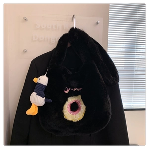 Detail of black plush tote bag with donut embroidery and cute white duck charm accessory