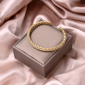 Detailed close-up of golden braided mesh cuff bracelet on elegant silk background